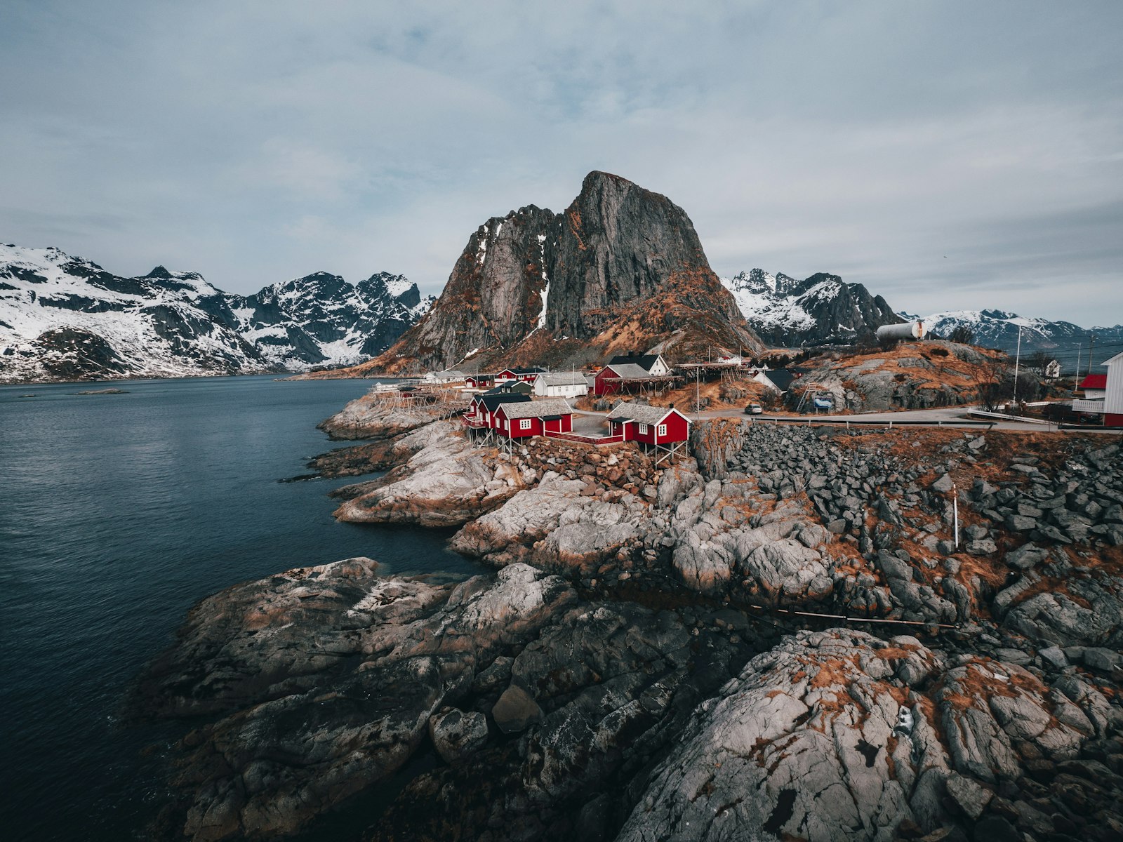 Nordic fjord landscape with red seaside cabins and mountains.